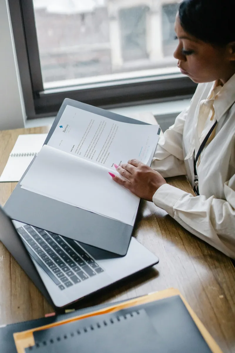 Une femme examinant des documents près d’un ordinateur portable