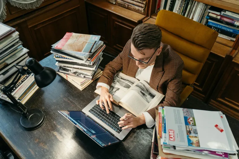 Un étudiant faisant des recherches avec livres et ordinateur dans une bibliothèque
