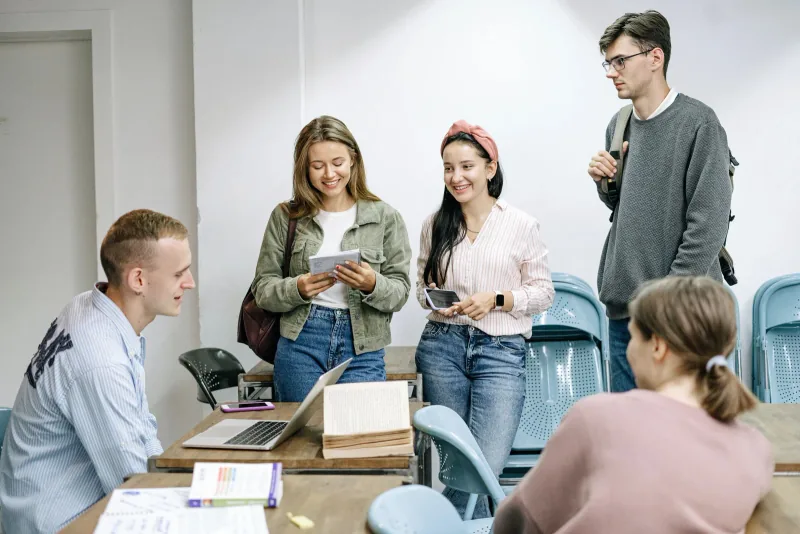 Des étudiants échangeant autour d’un bureau avec des livres et un ordinateur